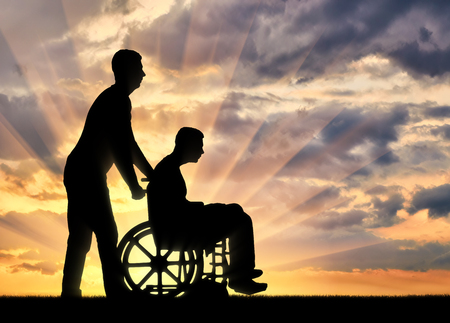 Silhouette of a disabled man in a wheelchair and a nurse in the sunset. The concept of caring for people with disabilitiesの写真素材