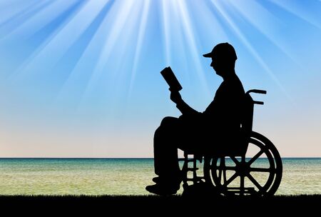 Silhouette of a disabled man in a wheelchair reading a book by the sea. Concept of the way of life of people with disabilitiesの写真素材