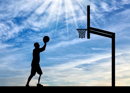 Silhouette of a disabled man with a leg prosthesis intends to throw the ball into the basket. The concept of people with leg prosthesis leading an active lifestyleの写真素材