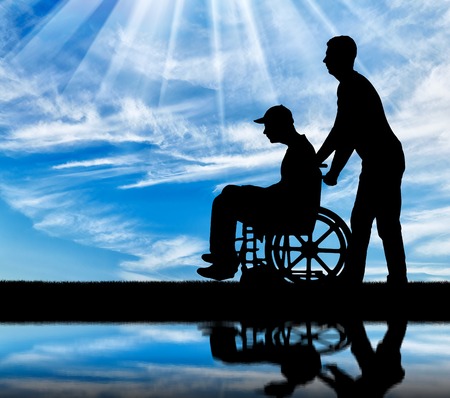 Silhouette of a walk of a disabled man in a wheelchair and a close person against the sky by the river. The concept of caring for people with disabilitiesの写真素材