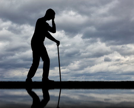 Silhouette of a sad disabled man with a cane in his hand by the river and his reflection.の写真素材