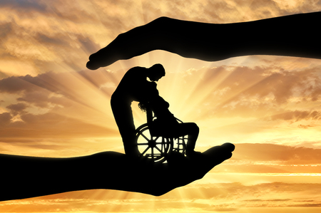 Silhouettes of a happy disabled woman in a wheelchair with a man who kisses her. The concept of support and assistance for people with disabilitiesの写真素材