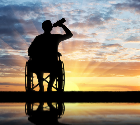 Silhouette of a disabled man in a wheelchair drinking water from a plastic bottle. Concept of leisure and recreation for disabled peopleの写真素材