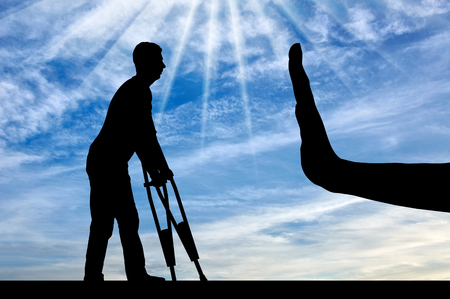 A silhouette of a man with crutches and a hand gesture of stop. The concept of discrimination and disrespect for people with disabilitiesの写真素材