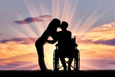 Silhouette of a disabled man in a wheelchair and his wife who is kissing. The concept of caring and supporting disabled peopleの写真素材