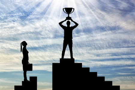Silhouette of a male winner with a trophy on the career ladder against the background of a woman who has no chance of winning. The concept of gender inequality and discriminationの写真素材
