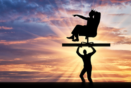 The silhouette of a selfish man with a crown on his head sitting in a chair, points to another man who carries it, where to move. The concept of selfish behavior towards other peopleの写真素材