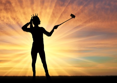 A silhouette of a narcissistic and selfish woman with a crown on her head, makes selfie on the phone. The concept of narcissism and selfishnessの写真素材