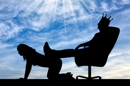 Silhouette of a selfish man with a crown on his head sitting in a chair, threw back his legs on the woman's back. The concept of discrimination and inequality to womenの写真素材