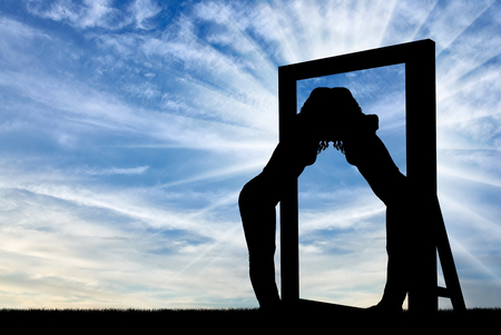 Silhouette of a narcissistic woman hugging her reflection in a mirror. The concept of narcissism and selfishnessの写真素材