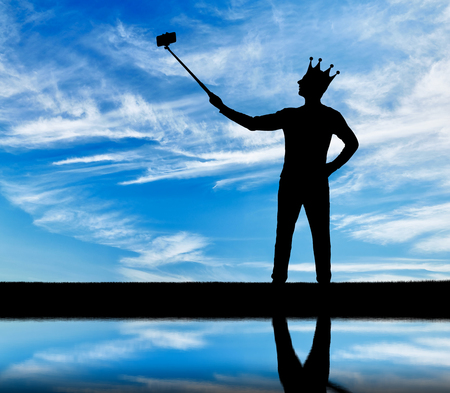 Silhouette of a narcissistic and selfish man with a crown on his head, makes selfie on the phone. The concept of narcissism and selfishnessの写真素材