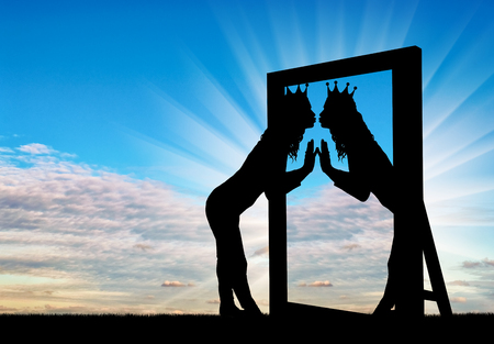 A silhouette of a narcissistic woman with a crown on her head kisses her reflection in the mirror. The concept of narcissism and selfishnessの写真素材