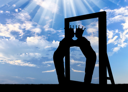 Silhouette of a narcissistic man with a crown on his head hugging his reflection in the mirror. The concept of narcissism and selfishnessの写真素材