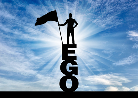 Silhouette of a selfish man who holds a flag on top of the word ego. The concept of selfishness and narcissismの写真素材