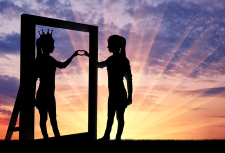 Silhouette of a narcissistic woman with a crown on her head and a hand gesture of the heart in reflection in the mirror. The concept of narcissism and selfishnessの写真素材