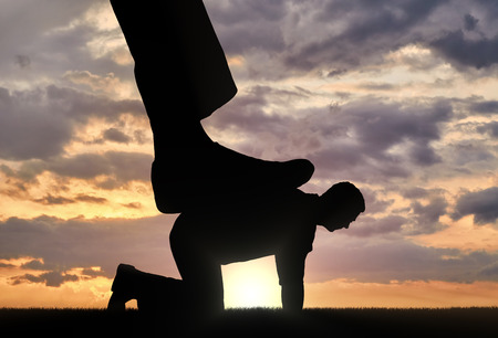 Silhouette of a large leg pressing on a man who fell on all fours. The concept of humiliation of human dignityの写真素材