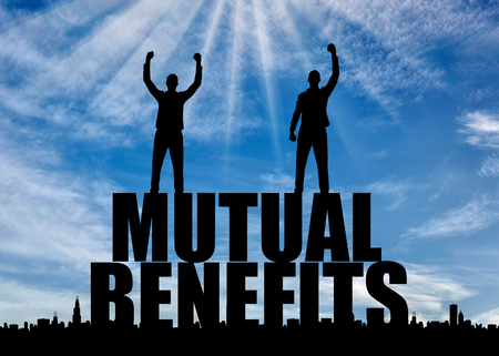 Silhouette of two happy men with raised arms standing on the word mutual benefit. The concept of mutual benefitの写真素材