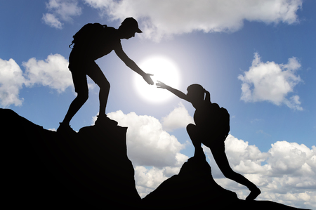 Silhouette climber man helping a woman climber to overcome the obstacle. Conceptual image of a helping handの写真素材