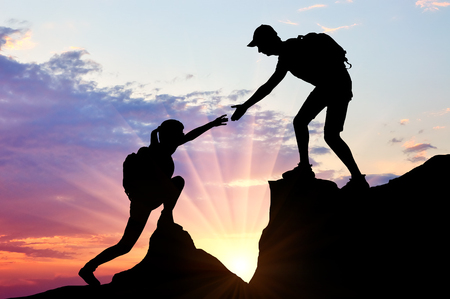 Silhouette of a male climber giving a helping hand to a woman. Conceptual image teamworkの写真素材