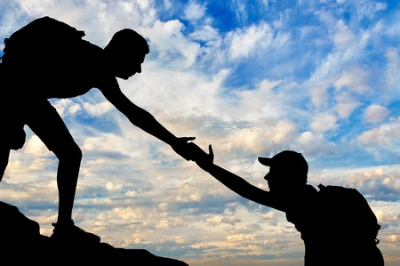 Silhouette of a male mountaineer giving a helping hand to his partner. The concept of teamworkの写真素材
