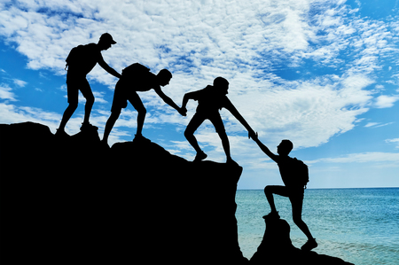 Men climbers help each other in the mountains against the background of the sea. Conceptual scene of male mountaineers work in a teamの写真素材