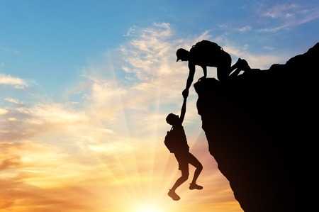 Silhouette of a climber saves another climber pulling him from the abyss. Conceptual Sceneの写真素材