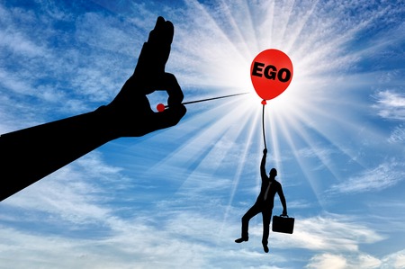 A selfish businessman clings to a balloon called the ego and a big hand with a needle intends to burst it. Conceptual scene the higher you fly the harder they fallの写真素材