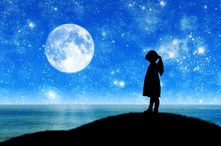 Silhouette, little girl child standing on a hill by the sea looking at the starry sky. Conceptual image of children's dreamsの写真素材