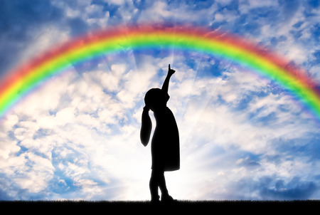 Silhouette of a baby girl showing a finger in the sky on a rainbow. Conceptual childhood sceneの写真素材