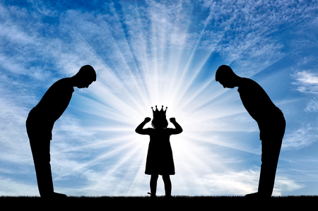 Selfish little girl with a crown on her head and two servants worship her. Concept of selfish and narcissistic childrenの写真素材