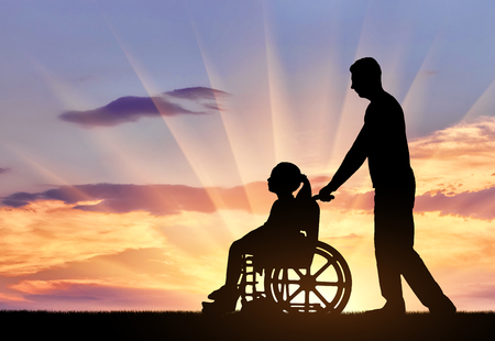 Silhouette of a disabled child girl sitting in a wheelchair and her dad on a walk. The concept of helping and caring for children with disabilitiesの写真素材