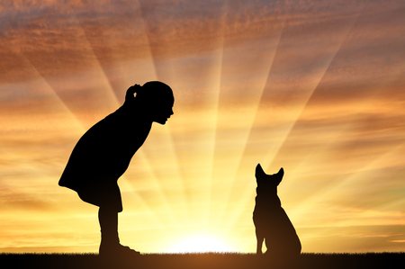 Silhouette of a baby girl and her dog looking at the sunset. The concept of children and their petsの写真素材