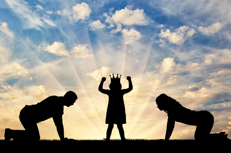 Silhouette of a child girl with a crown on her head and parents worshiping her. Conceptual image of childish egoismの写真素材