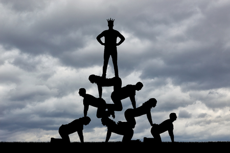 Silhouette of a narcissist male businessman selfish with a crown on his head is standing on people. The concept of selfish and narcissist bossの写真素材