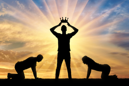 Silhouette of a woman and a man worshiping a man who puts a crown on his head against the sunset. The concept of a selfish and arrogant personの写真素材