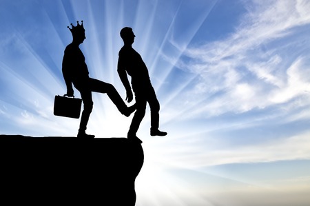 Silhouette, A male egoist with a crown is pushing another man into the abyss with his foot. Concept of selfishness and betrayal in businessの写真素材