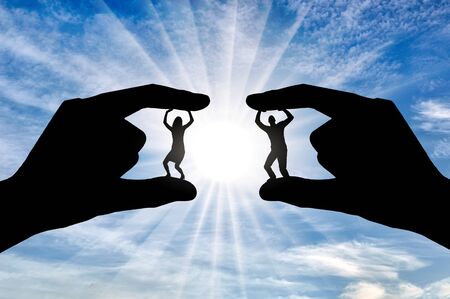 Workplace bullying concept. Silhouettes of two hands hold between the fingers a man and a woman. Fingers intend to crush them.の写真素材