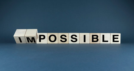 A minimalist image of wooden blocks arranged to form the words IMPOSSIBLE and POSSIBLE. The image visually represents the concept of shifting one's perspective and overcoming challengesの写真素材