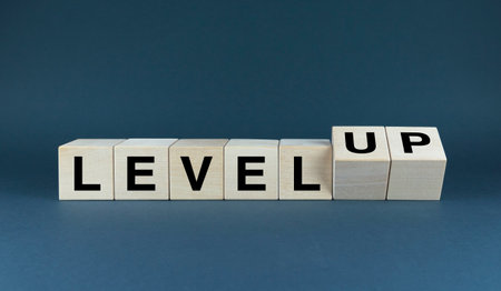 A minimalist image of wooden blocks spelling LEVEL and then LEVEL UP. The image represents the concept of growth, progress, and achieving new heightsの写真素材