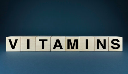 Word VITAMINS spelled out on wooden blocks against a dark background. This image visually represents the essential role of vitamins in maintaining good health. It can be used in various health-related projects, including nutrition education, dietary supplements, and wellness campaignsの写真素材
