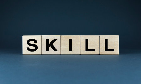 A set of wooden cubes spelling out the word SKILL against a dark blue background. The image symbolizes the importance of developing skills to achieve success in any endeavorの写真素材