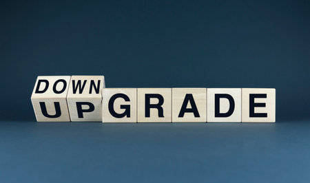 A conceptual image featuring wooden blocks spelling out the words upgrade and downgrade. The first two blocks are positioned at an angle, suggesting a choice or decision between the two optionsの写真素材