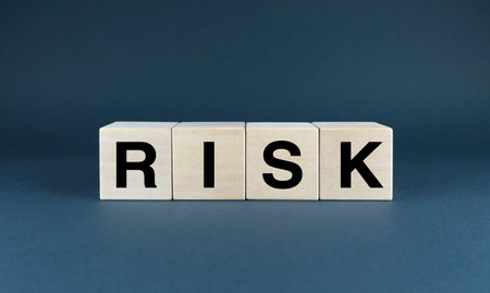 A minimalist conceptual image featuring wooden blocks spelling out the word RISK against a dark blue background. This image visually represents the concept of uncertainty and the potential dangers that lie aheadの写真素材