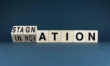 image of wooden blocks spelling out the words stagnation and innovation, with the stagnation blocks being flipped over to reveal the innovation blocks. The image represents the concept of overcoming stagnation and embracing innovationの写真素材