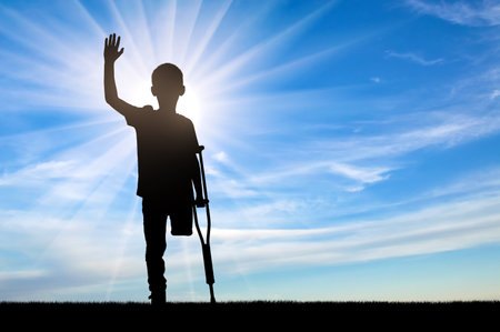 A silhouette of a disabled child with crutches, against a sunny sky, representing hope, strength and a spirit of perseverance. Perfect for themes of courage and determination that children who face physical challenges show.の写真素材
