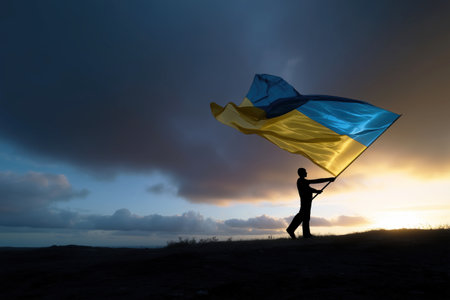 Person holds the Ukrainian national flag, illuminated against a twilight backdrop, symbolizing resilience, patriotism, and support for Ukraine in challenging times.の素材