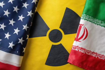 Symbolic representation of the escalating US and Iranian nuclear conflict, showing the American and Iranian flags alongside a radioactive symbol.の素材