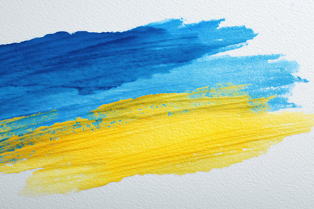 An abstract watercolor brush stroke pattern in the colors of Ukraine flag; blue and yellow paints running together on textured white paper.の素材