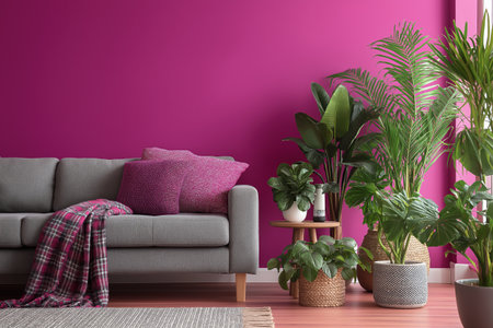 A chic contemporary living room featuring a comfortable gray sofa with magenta pillows and a plaid throw, set against a bold pink wall with lush green plants.の素材
