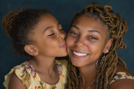 A close-up portrait of a happy black mother receiving a loving kiss from her cute little girl. A heartwarming moment of family love and tenderness.の素材